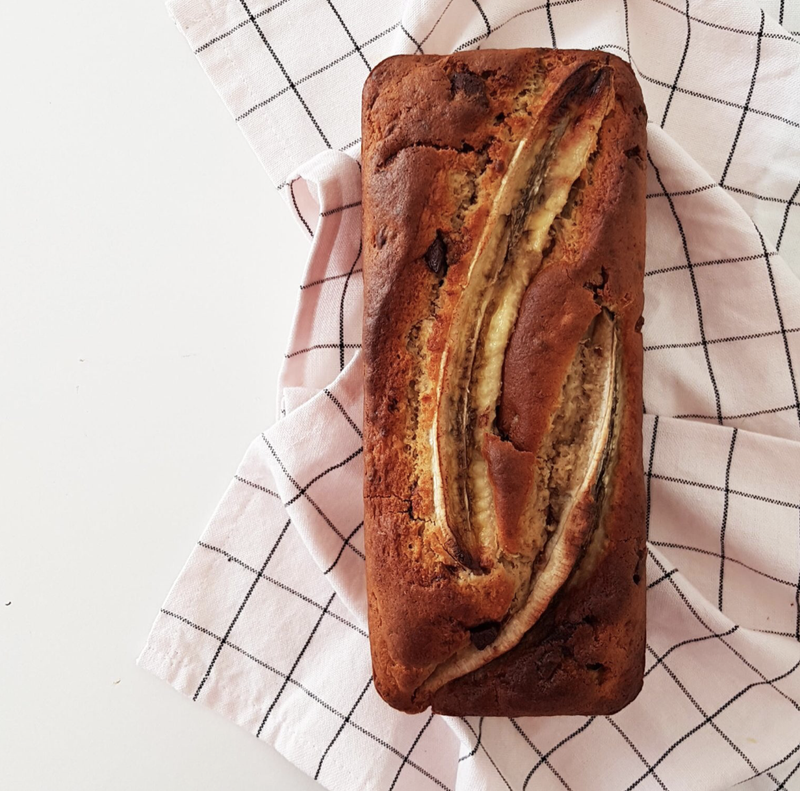 a chocolate banana bread on a kitchen towel, view from top. Two
half-bananas are visible on top. Chocolate chunks visible on the cake.